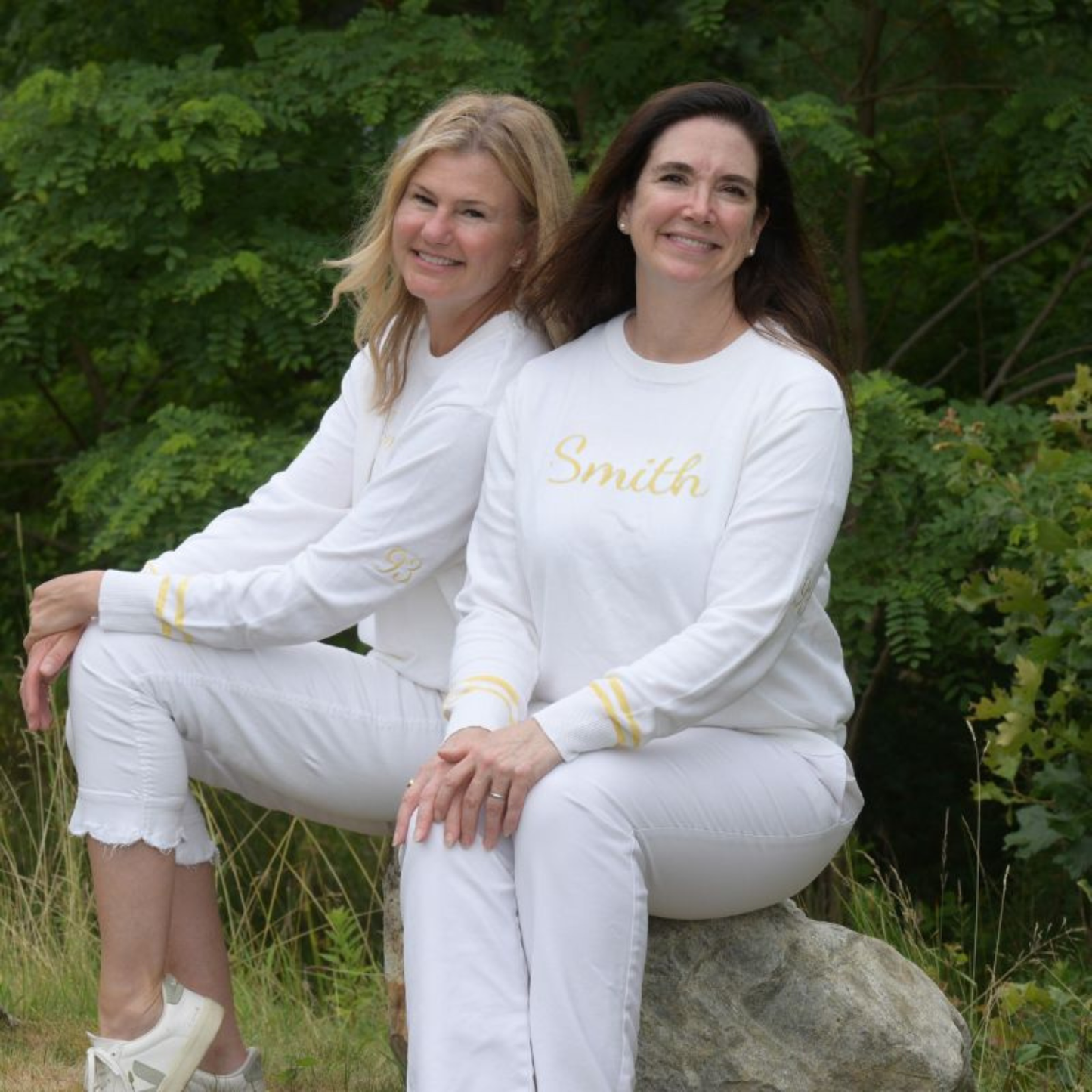 Two women in matching white outfits with 'Smith' embroidered on their shirts, sitting outdoors.