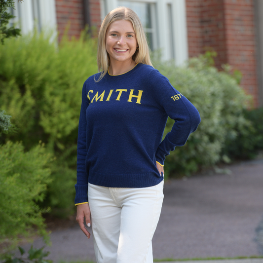 Woman wearing a navy sweater with 'SMITH' printed on it, standing outdoors.