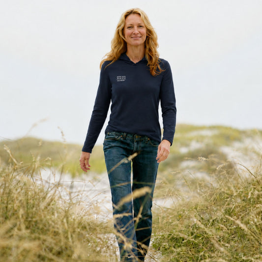 A woman walking outdoors in a grassy field wearing a navy blue long-sleeve quarter-zip pullover with a small white logo on the left chest, paired with blue jeans.