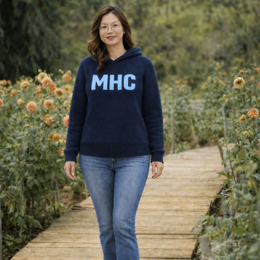 Woman wearing a navy blue hoodie with 'MHC' on it, standing on a wooden path in a garden.