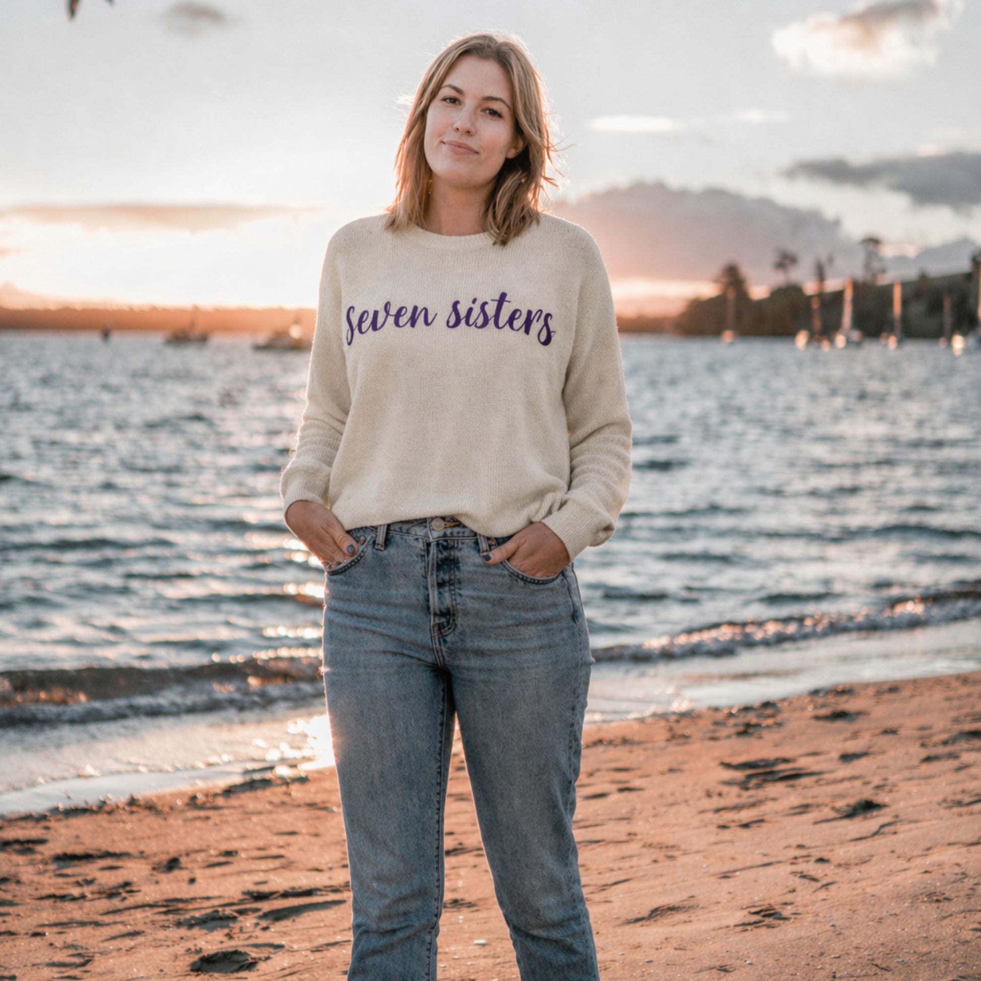Woman wearing a 'Seven Sisters' sweater on a beach at sunset