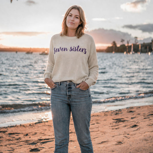 Woman wearing a 'Seven Sisters' sweater on a beach at sunset